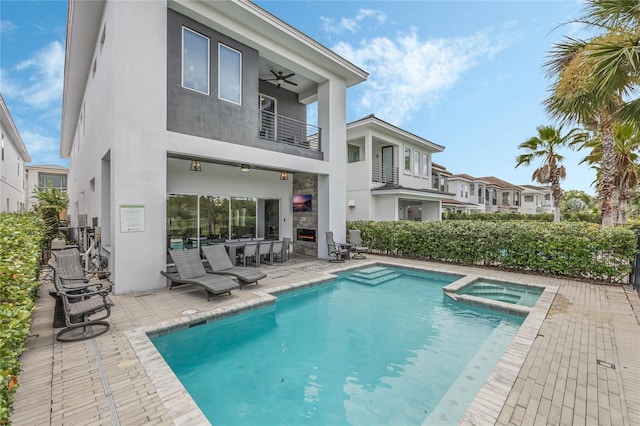 back of property featuring ceiling fan, a swimming pool with hot tub, a balcony, and a patio