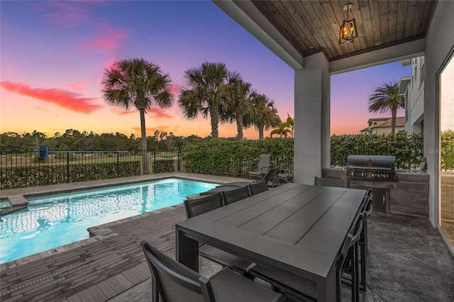 pool at dusk with grilling area and an outdoor kitchen