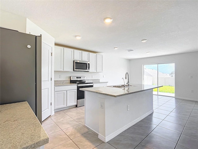 kitchen with sink, light tile patterned floors, stainless steel appliances, white cabinets, and a center island with sink