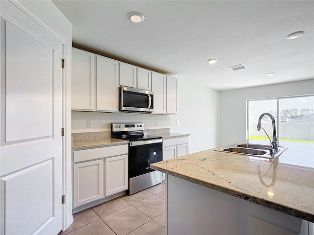 kitchen featuring light tile patterned floors, white cabinets, appliances with stainless steel finishes, and a sink