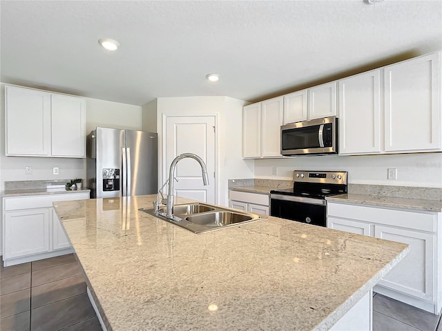 kitchen with a center island with sink, a sink, white cabinetry, stainless steel appliances, and tile patterned flooring