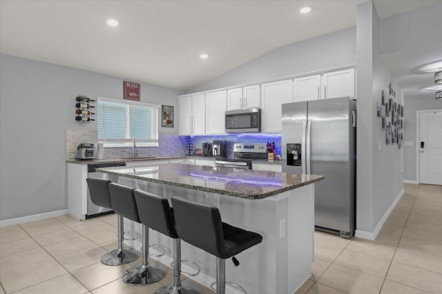 kitchen with white cabinets, a kitchen island, stainless steel appliances, and vaulted ceiling