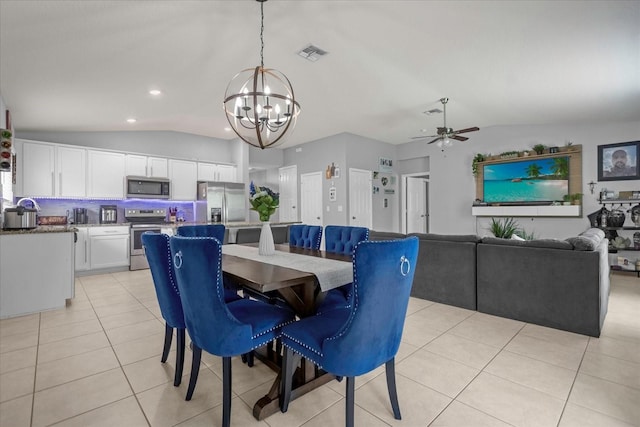 dining space with ceiling fan with notable chandelier, light tile patterned floors, and vaulted ceiling