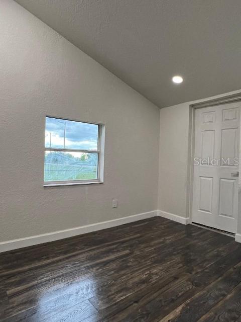 empty room with dark hardwood / wood-style flooring and vaulted ceiling