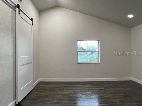 unfurnished room with a barn door, dark hardwood / wood-style flooring, and lofted ceiling