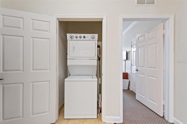 laundry room with crown molding, light tile floors, and stacked washer / drying machine