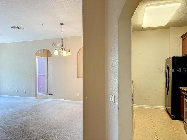 hallway with light colored carpet and a chandelier