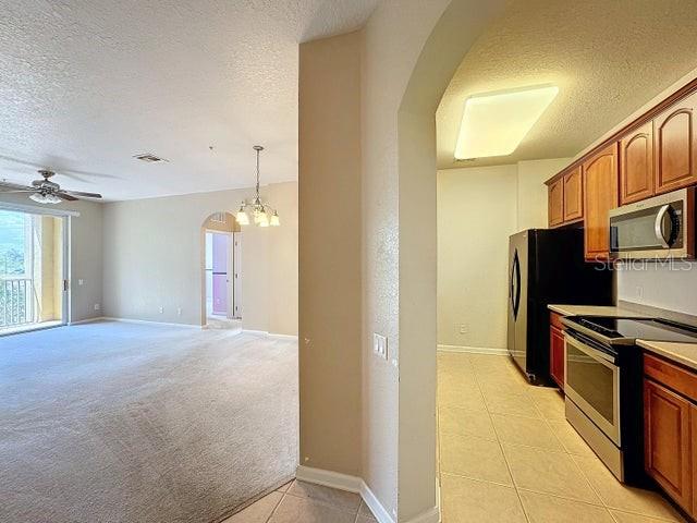 kitchen with light carpet, decorative light fixtures, ceiling fan with notable chandelier, a textured ceiling, and appliances with stainless steel finishes