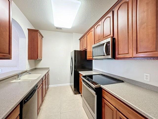 kitchen with light tile patterned floors, brown cabinetry, stainless steel appliances, light countertops, and a sink