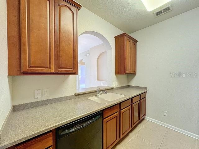 kitchen featuring dishwasher, sink, a textured ceiling, and light tile floors