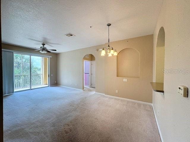 spare room featuring a textured ceiling, carpet flooring, and ceiling fan with notable chandelier