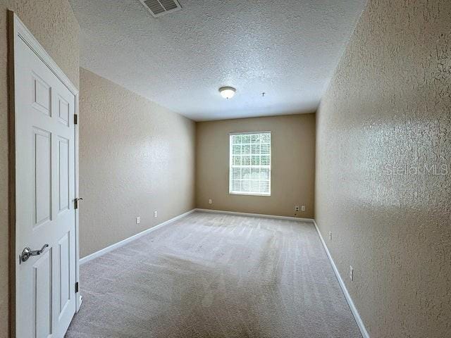 spare room with light colored carpet, visible vents, a textured wall, a textured ceiling, and baseboards