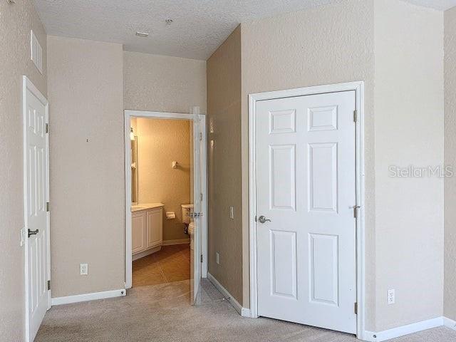 unfurnished bedroom featuring a textured ceiling, ensuite bath, and light colored carpet