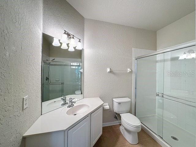 bathroom with tile flooring, walk in shower, a textured ceiling, toilet, and vanity