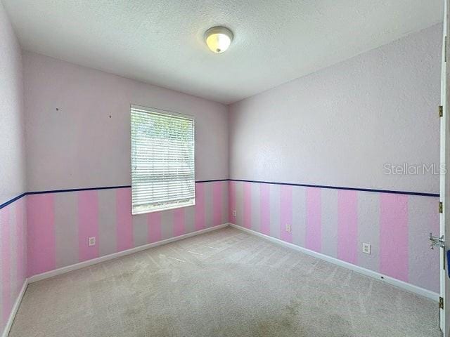 unfurnished room featuring light carpet, a textured ceiling, and baseboards