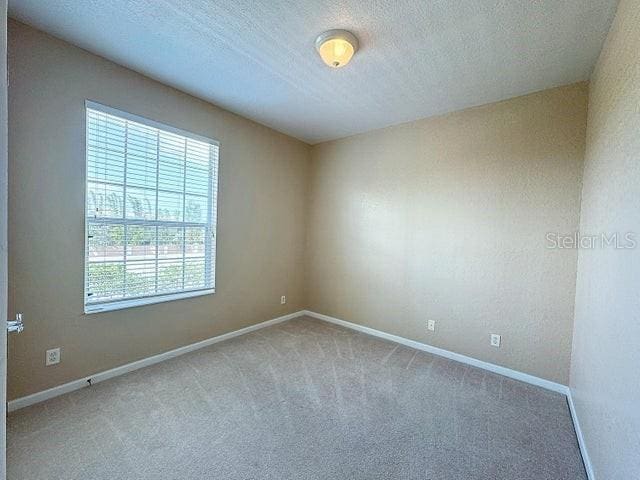 carpeted spare room featuring a textured ceiling and baseboards