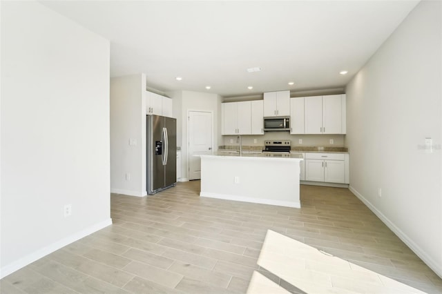 kitchen with white cabinetry, appliances with stainless steel finishes, a kitchen island with sink, and sink