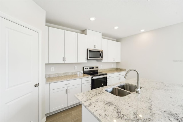 kitchen with white cabinets, sink, appliances with stainless steel finishes, light stone countertops, and light hardwood / wood-style floors