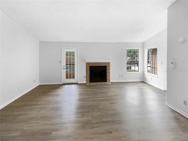 unfurnished living room with lofted ceiling, a tile fireplace, and dark wood-type flooring