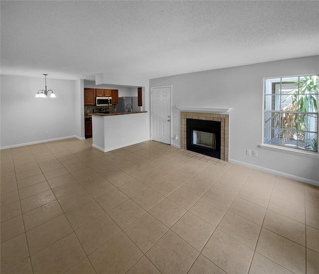 unfurnished living room with a tile fireplace, light tile patterned floors, a textured ceiling, and an inviting chandelier