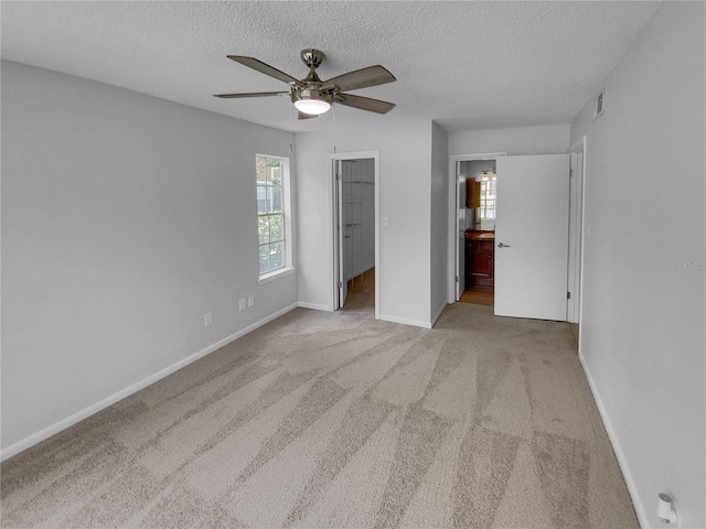 unfurnished bedroom featuring ensuite bath, ceiling fan, a spacious closet, light colored carpet, and a closet