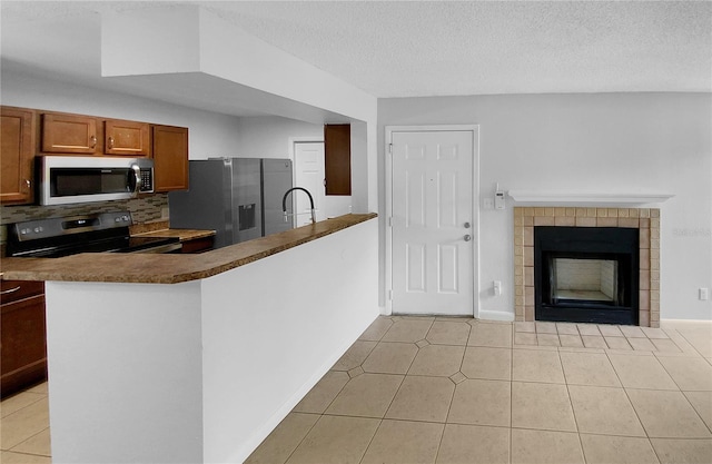 kitchen with decorative backsplash, a textured ceiling, stainless steel appliances, light tile patterned floors, and a fireplace