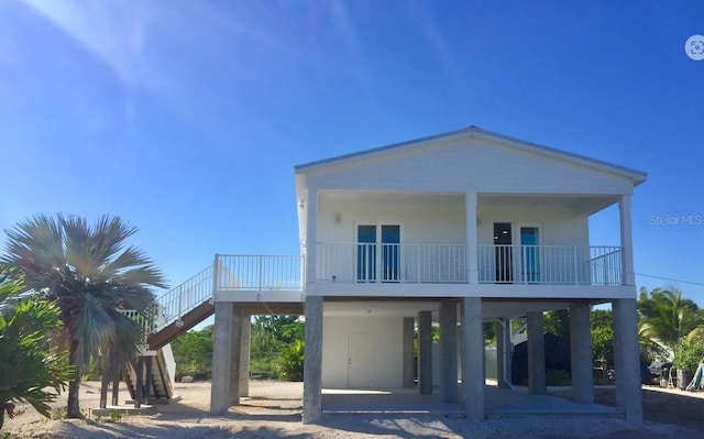 coastal inspired home with dirt driveway, a carport, and stairs