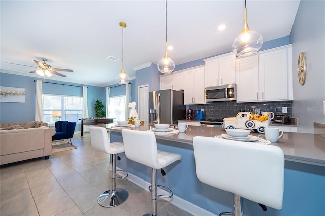 kitchen with hanging light fixtures, ornamental molding, a kitchen bar, white cabinetry, and stainless steel appliances