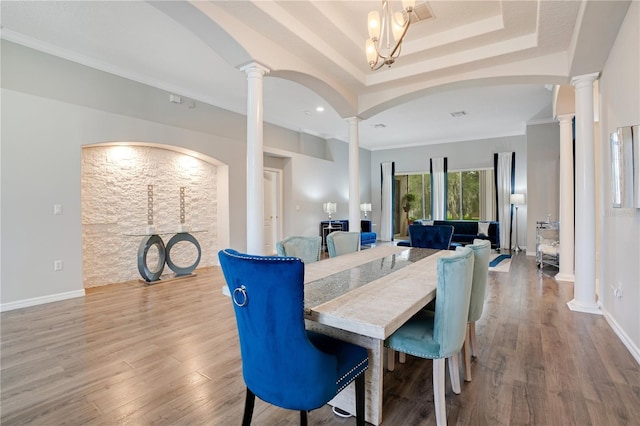 dining area featuring decorative columns, crown molding, hardwood / wood-style floors, and a tray ceiling