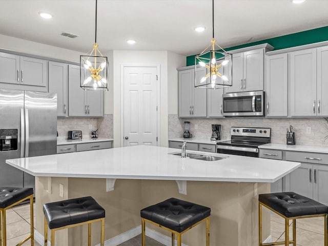 kitchen with a kitchen bar, stainless steel appliances, sink, hanging light fixtures, and an island with sink