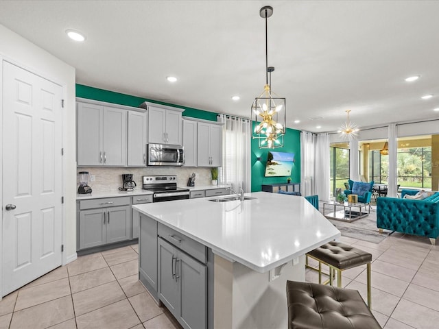 kitchen featuring stainless steel appliances, tasteful backsplash, an island with sink, a chandelier, and light tile patterned floors