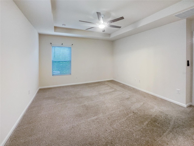 carpeted spare room with a raised ceiling and ceiling fan