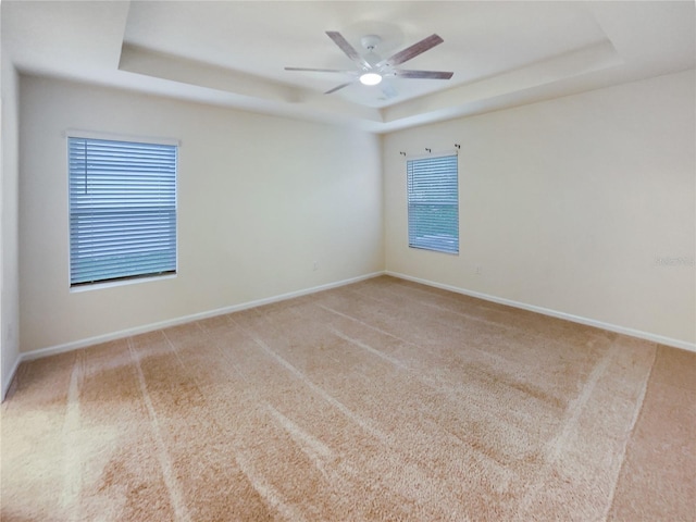 spare room with light carpet, a tray ceiling, and ceiling fan