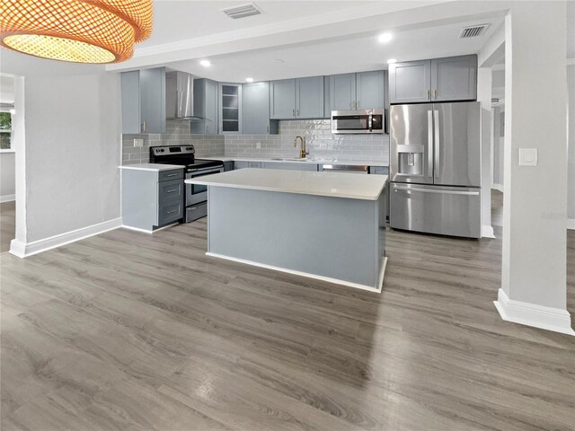 kitchen with appliances with stainless steel finishes, decorative light fixtures, gray cabinets, and wall chimney range hood