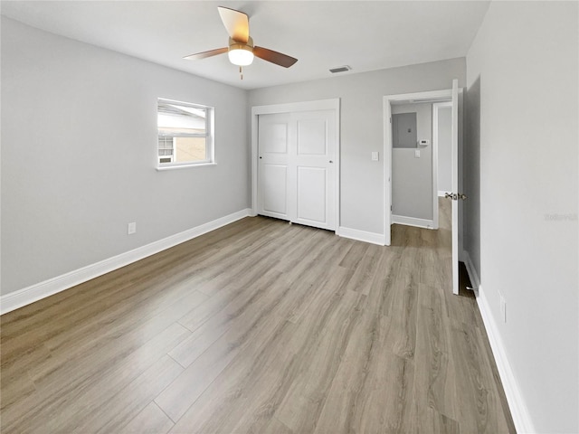 unfurnished bedroom featuring ceiling fan, light hardwood / wood-style flooring, electric panel, and a closet