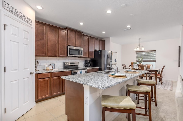 kitchen with sink, hanging light fixtures, a kitchen island with sink, stainless steel appliances, and a chandelier