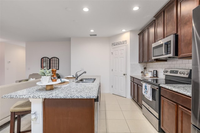 kitchen featuring light stone countertops, stainless steel appliances, sink, and an island with sink