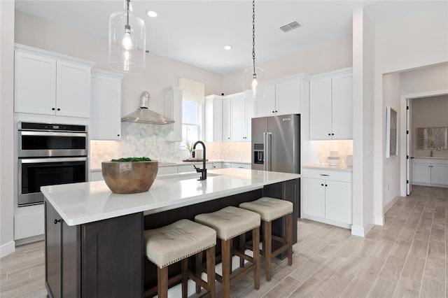 kitchen with white cabinetry, a kitchen island with sink, decorative light fixtures, and appliances with stainless steel finishes