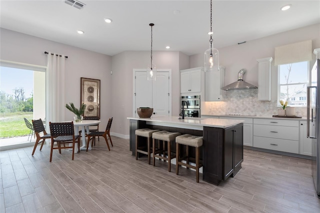 kitchen featuring decorative light fixtures, decorative backsplash, a breakfast bar, white cabinets, and a center island with sink