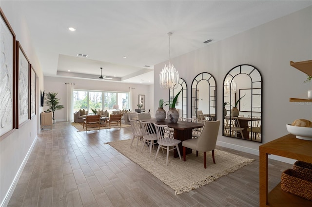 dining room with ceiling fan with notable chandelier and a tray ceiling