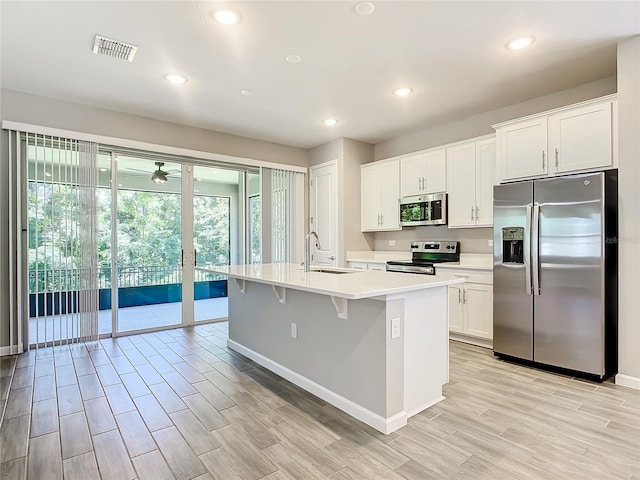 kitchen featuring white cabinets, a center island with sink, sink, a kitchen bar, and stainless steel appliances