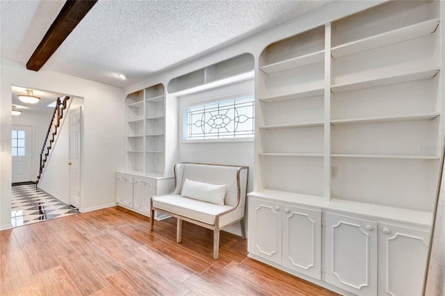 unfurnished room featuring light wood finished floors, stairs, beam ceiling, and a textured ceiling