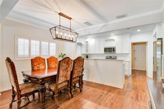 dining space with light wood-style floors, visible vents, and crown molding