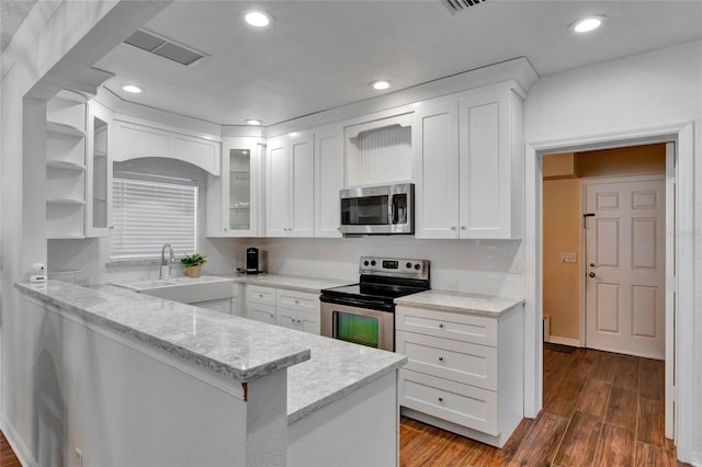 kitchen with a peninsula, white cabinetry, appliances with stainless steel finishes, light stone countertops, and glass insert cabinets