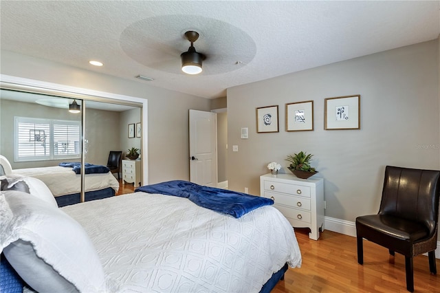 bedroom featuring a textured ceiling, ceiling fan, a closet, and light hardwood / wood-style flooring