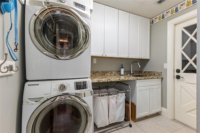 washroom with a textured ceiling, cabinets, sink, stacked washing maching and dryer, and light tile patterned floors