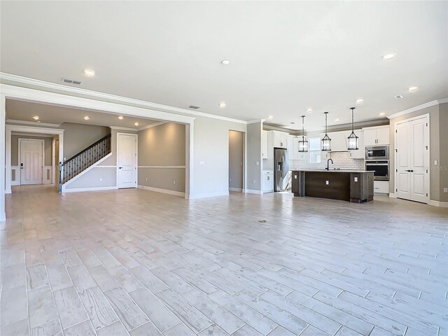 unfurnished living room featuring ornamental molding, sink, and light wood-type flooring