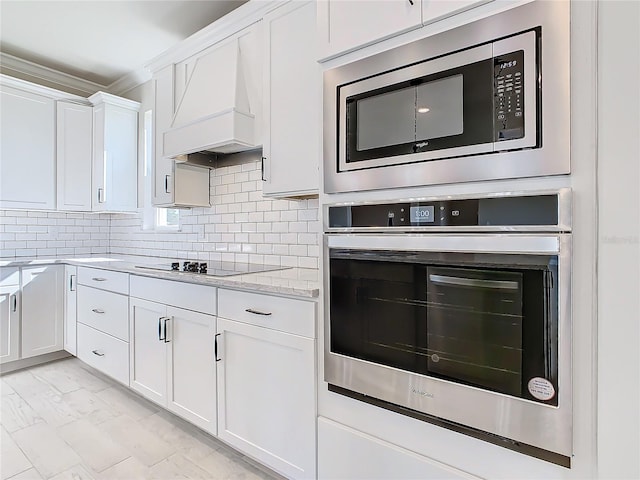 kitchen featuring premium range hood, white cabinetry, appliances with stainless steel finishes, light stone counters, and tasteful backsplash