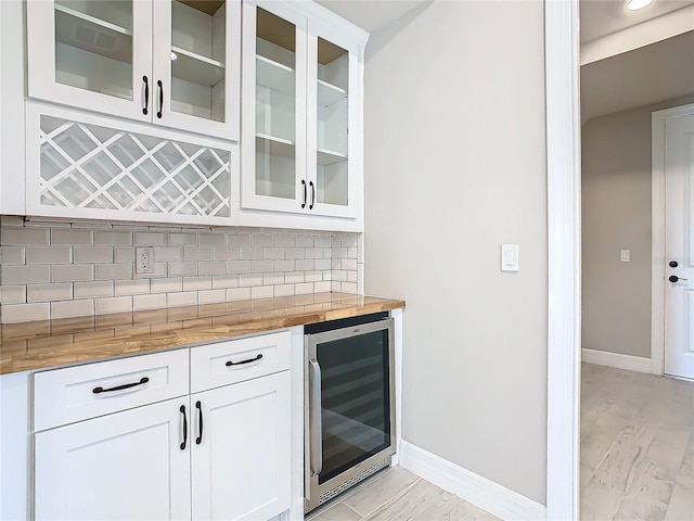 bar with white cabinets, beverage cooler, backsplash, light hardwood / wood-style floors, and light stone countertops