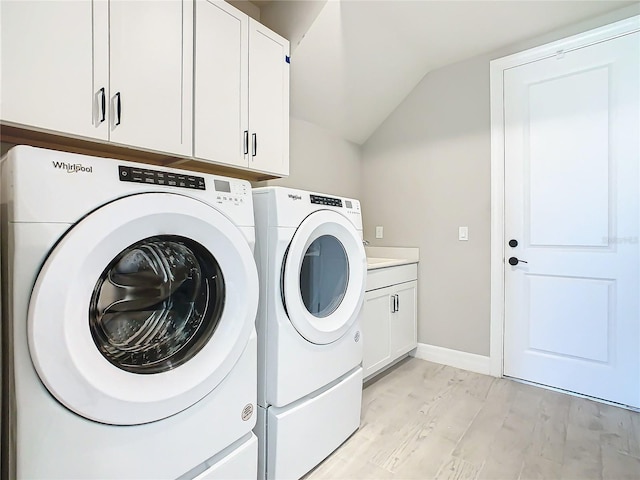 clothes washing area with cabinets, washer and clothes dryer, and light hardwood / wood-style flooring